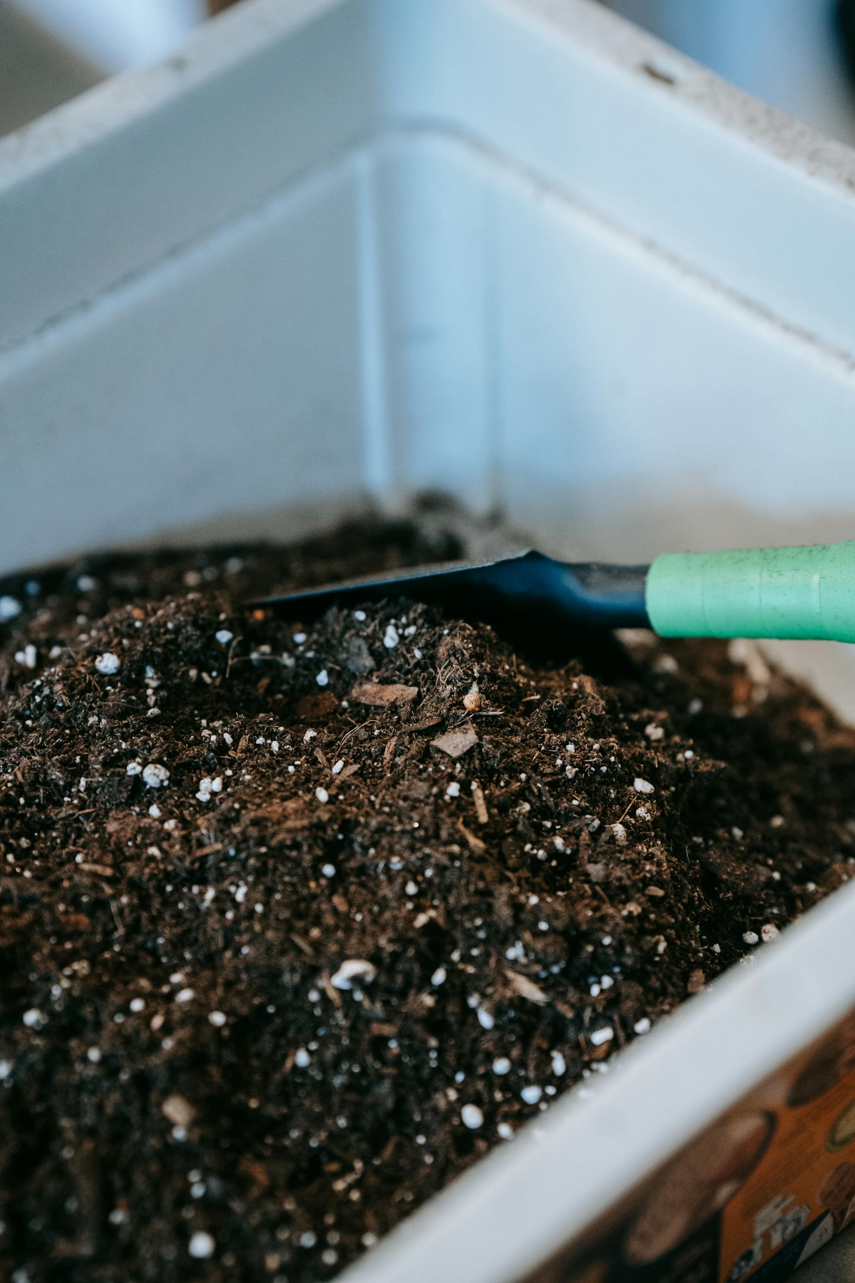 Gardening soil with a green-handled trowel in a white container, perfect for planting.